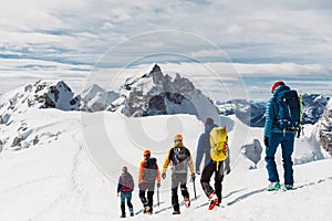 View from the back, five mountaineers descending down the snowy mountain, walking in a row