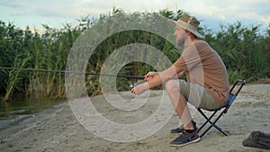 the view from the back is a man fisherman at dawn on the lake catching fish with a bait. Side view sitting on a chair