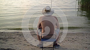 the view from the back is a man fisherman at dawn on the lake catching fish with a bait. sits on a chair and waits for a