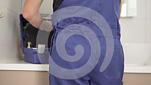 View from the back, a man in a plumbing suit pulls tools from a work suitcase