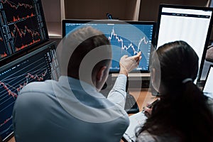 View from the back. Team of stockbrokers are having a conversation in a office with multiple display screens