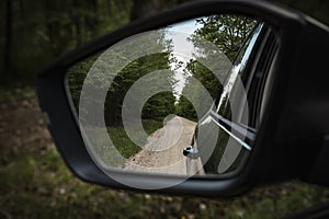 View back  to the gravel dirt road passing through dense forest in the rearviewmirror