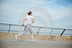 View from the back to a sportswoman, runner jogger athlete doing cardio workout, running outdoors on the city bridge