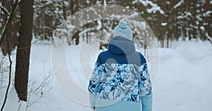 A view from the back of a woman in a blue tracksuit who is skiing in the forest