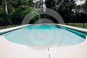 View of backyard swimming pool outside of a home with a large lot. There is a black metal fence