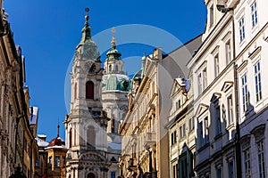 View of Baroque Church of Saint Nicholas, green dome and bell tower with clock, sunny winter day, snow on red roofs, Mala Strana