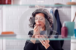 View Through Bathroom Cabinet As Businesswoman Checks Messages On Mobile Phone And Puts On Lipstick