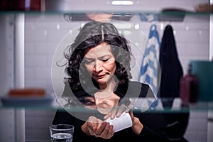 View Through Bathroom Cabinet Of Mature Woman Taking Medication From Container