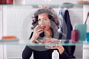 View Through Bathroom Cabinet Of Mature Woman Taking Medication With Glass Of Water