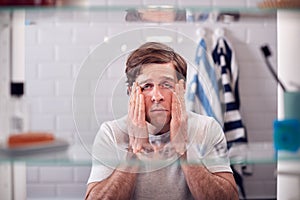 View Through Bathroom Cabinet Of Tired Man Looking In Mirror Before Going To Work