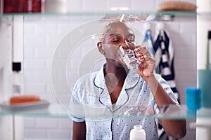 View Through Bathroom Cabinet Of Woman Drinking Glass Of Water