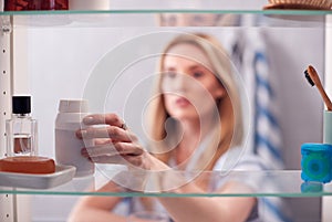 View Through Bathroom Cabinet Of Young Woman Taking Medication From Container