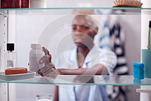 View Through Bathroom Cabinet Of Young Woman Taking Medication From Container