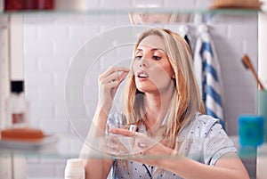 View Through Bathroom Cabinet Of Young Woman Taking Medication With Glass Of Water