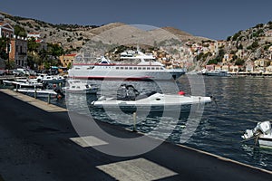 View of the bay of Symi island. A ship, passenger boats and yachts on a background of hills. Shadow and light on the water