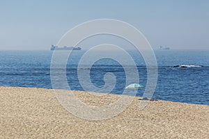 View of beach with clean sand, beach parasol, on the beach, with towel, sea with wave, boat and ship, sky with seagull as