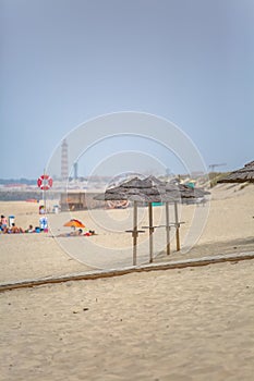 View of a beach with four straw parasol, summer weather with tourist people taking sunbathing