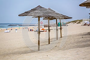 View of a beach with four straw parasol, summer weather with tourist people taking sunbathing photo