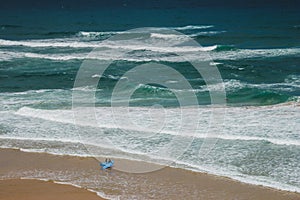 View of beach with large waves near Atlantic coast. Surfers on the ocean coast with surfboard. Praia Grande, Sintra, Portugal. Act