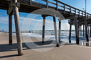 View of the beach and ocean from underneath a wooden pier through the wooden support pilings