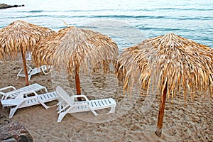 View of beach with straw umbrellas and lounges.