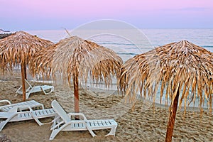 View of beach with straw umbrellas and lounges.