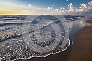 View from the beach on the white foam cups of the rising waves at high tide in the North Sea, all this at sunset