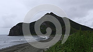 View of beautiful beach with green grass and mountain. Clip. Picturesque landscape with green grass on background of sea