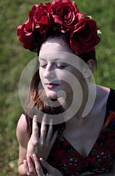 View of a beautiful, dreaming girl with closed eyes, who has a beautiful red wreath on her head with large flowers