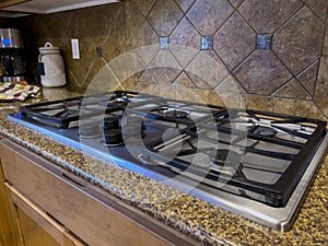 view of a beautiful gas stove top with black knobs against a square tiled backsplash