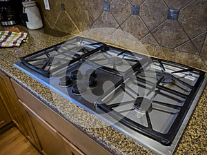 view of a beautiful gas stove top with black knobs against a square tiled backsplash