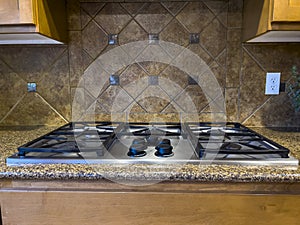 view of a beautiful gas stove top with black knobs against a square tiled backsplash