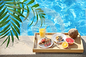 View of beautiful green tropical leaves and tray with delicious breakfast near swimming pool