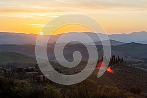 A view of a beautiful hilly Tuscan field in the golden morning light with a cypress farmhouse and hay bales in Italy