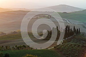 A view of a beautiful hilly Tuscan field in the golden morning light with a cypress farmhouse and hay bales in Italy