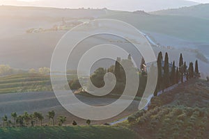 A view of a beautiful hilly Tuscan field in the golden morning light with a cypress farmhouse and hay bales in Italy