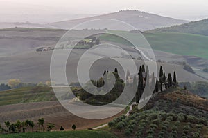 A view of a beautiful hilly Tuscan field in the golden morning light with a cypress farmhouse and hay bales in Italy