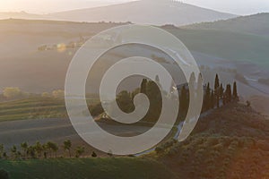 A view of a beautiful hilly Tuscan field in the golden morning light with a cypress farmhouse and hay bales in Italy