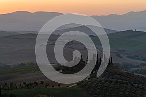 A view of a beautiful hilly Tuscan field in the golden morning light with a cypress farmhouse and hay bales in Italy