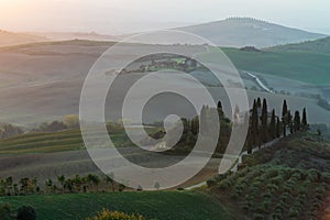 A view of a beautiful hilly Tuscan field in the golden morning light with a cypress farmhouse and hay bales in Italy