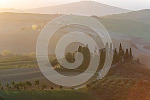 A view of a beautiful hilly Tuscan field in the golden morning light with a cypress farmhouse and hay bales in Italy