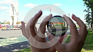 View of a beautiful multi-colored building through round tinted glass. Women's hands twist the ND filter and it