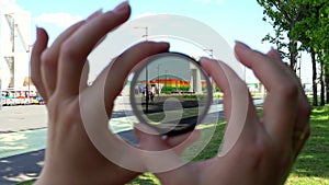 View of a beautiful multi-colored building through round tinted glass. Women's hands twist the ND filter and it