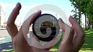 View of a beautiful multi-colored building through round tinted glass. Women's hands twist the ND filter and it