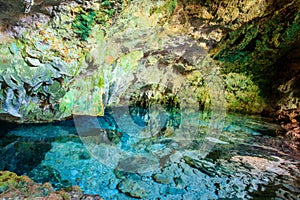 View of beautiful natural pool of crystal clear water formed in a rocky cave with stalagmites and stalagmites. Kuza cave