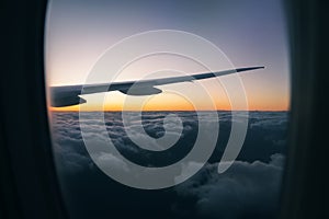 View of the beautiful sunset over the clouds from the window of the aircraft during the flight. Inside the cabin