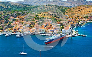 View on beautiful traditional Greek houses on Symi island green hills, yacht sea port, tourist ferryboat at Aegean Sea blue bay. M