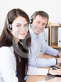 View of beautiful young businesswoman and handsome businessman in headsets using laptops in callcenter office