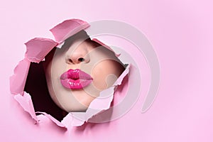 View of beautiful young woman with perfect lips makeup through hole in color paper