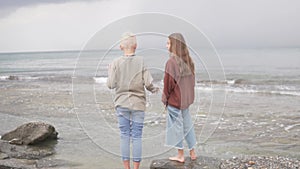 View from behind, beautiful teenage children look at the overcast sky on the sea